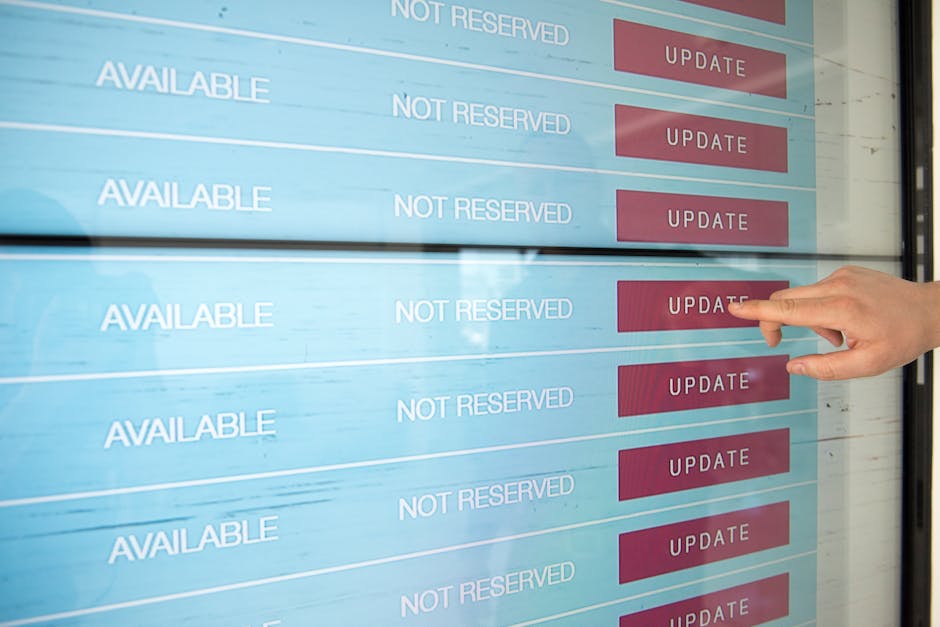 A person's hand is pointing to a red 'UPDATE' button on a digital display board featuring multiple rows of text. The board shows the words 'AVAILABLE' and 'NOT RESERVED' in white capital letters on a 